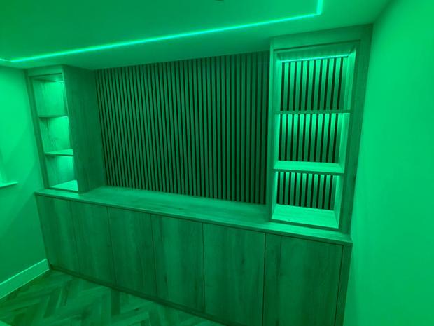 Full height fitted oak cabinetry under coloured lighting
